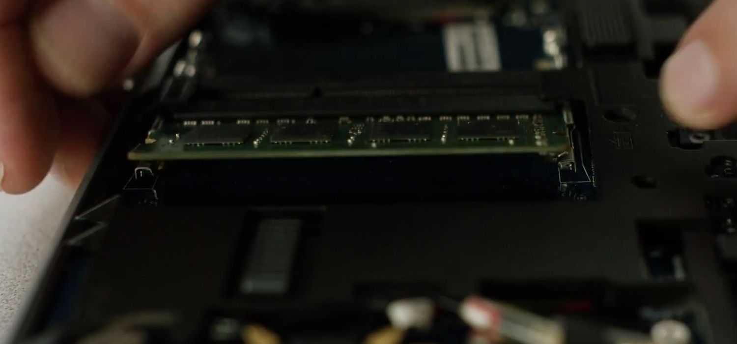 Una persona abre las pinzas laterales de un módulo RAM Crucial para quitarlo de la computadora portátil
